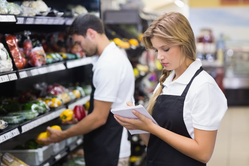 Serious staff woman wrting on notepad at supermarket